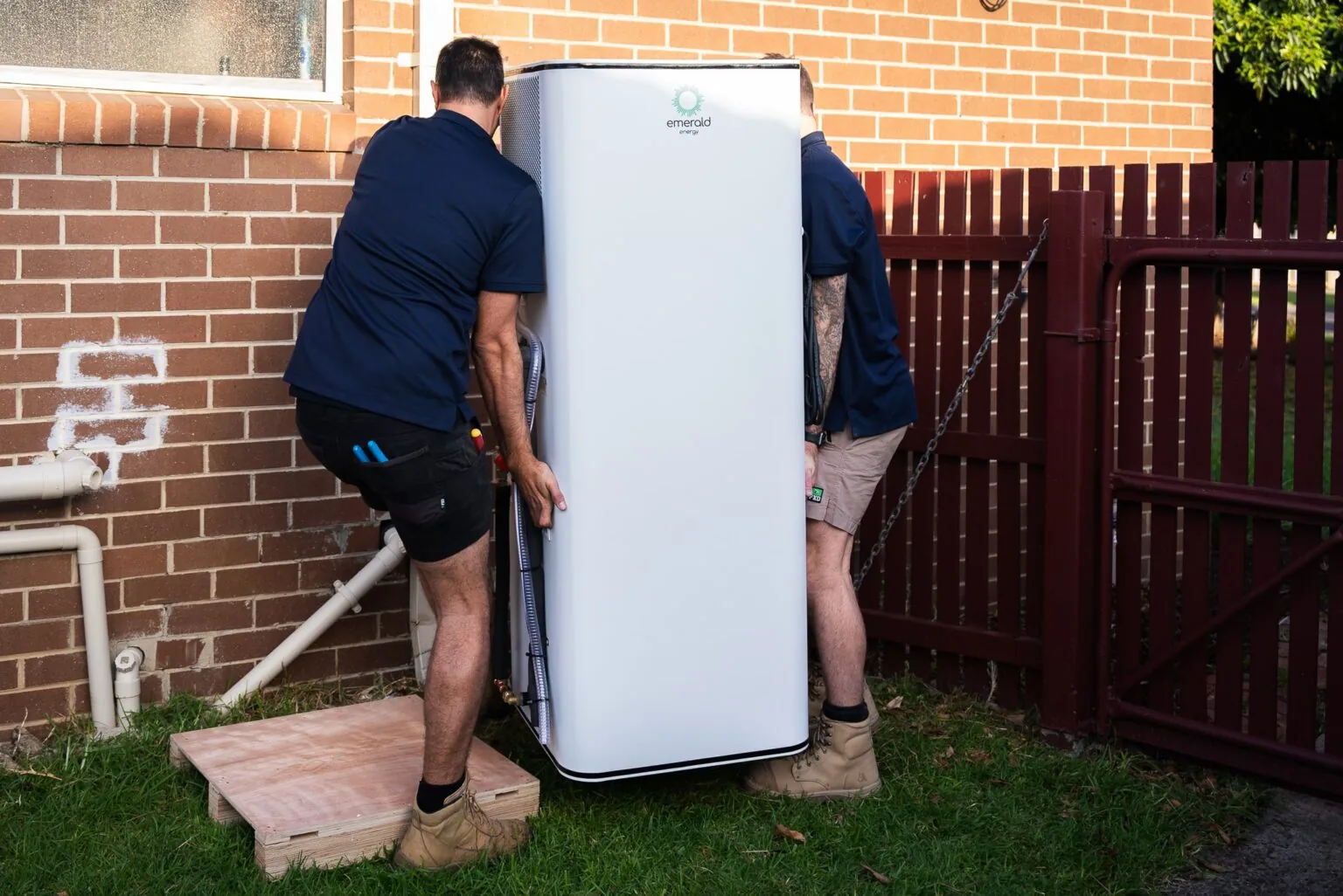 Installers positioning a heat pump hot water system outside a home
